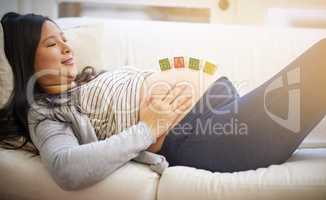 The pregnancy glow they all talk about. an attractive young pregnant woman balancing wooden blocks on her tummy while relaxing on the sofa at home.