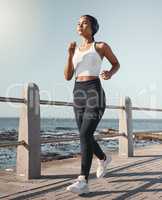 Young fit sportswoman wearing wireless headphones and listening to music while out for a run along the promenade. Exercise is good for you health and wellbeing