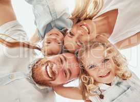 Bottom of happy family in a huddle. Faces of smiling mother and father with their cute daughters from below. Young woman and man having fun and playing with their little girls in a circle and hugging