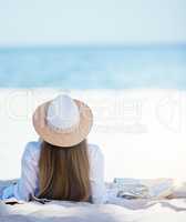 Rearview beautiful young caucasian woman relaxing on the beach. Enjoying a summer vacation or holiday outdoors during summer. Taking time off and getting away from it all. Spending the day alone