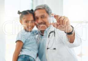 Itll keep you safe from future illness. Shot of a mature doctor holding a vaccine vial during a checkup with a little girl at home.