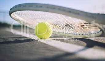 Below shot of a tennis racquet and tennis ball on a sports court. The only tools a professional tennis player needs to participate in their chosen sport. Six games per set to see who wins the match