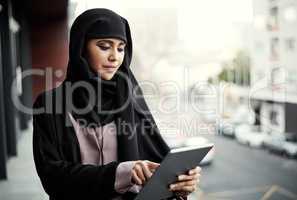 Shes working smart. an attractive young businesswoman dressed in Islamic traditional clothing using a tablet while standing on her office balcony.