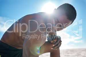 Fit young topless black man taking a break from his run or jog at the beach in the morning for exercise. One strong male bodybuilder athlete looking focused for his cardio and endurance workout