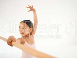 It takes practice to get better. a little girl practicing ballet at a barre in a dance studio.