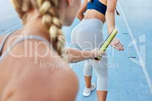 Relay race athlete handing the baton over to a teammate while running from behind. Rearview closeup of two female athletes working together as a team to compete in and win a sports competition