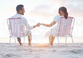 Distance will never decrease my love for you. Shot of a young couple holding hands while sitting on their beach chairs.