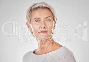 Beautiful serious mature caucasian woman isolated against a grey background in studio and posing. Portrait of confident senior woman with grey hair. Youthful skin comes from a healthy skincare routine