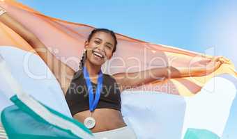 Portrait of a young fit indian female athlete cheering and holding India flag after competing in sports. Smiling fit active sporty woman feeling motivated and celebrating