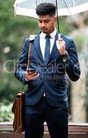 Nothing will damper his determination. a young businessman using a cellphone while holding an umbrella on a rainy day in the city.