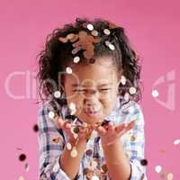 A pretty little mixed race girl with curly hair blowing confetti from her hands against a pink copyspace background in a studio. African child looking excited at a gender reveal party