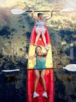 Above portrait of two diverse young women cheering and celebrating while canoeing on a lake. Excited friends enjoying rowing and kayaking on a river while on holiday or vacation on a weekend getaway