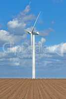 Wind turbines on a farm with newly planted crops. Cloudy day on agricultural land where wind energy is the main resource. Producing sustainable electricity and fresh produce