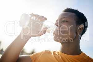 A jogger drinking a bottle of water in the sunlight. An active, healthy African American man quenching his thirst after exercising