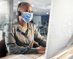 One african american call centre telemarketing agent wearing face mask as health and safety protocol talking on headset while using computer in an office. Female consultant operating helpdesk for customer service and sales support during covid pandemic