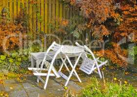 White wooden chairs and table in a serene, peaceful, lush, private backyard at home in autumn. Patio furniture set in outdoor space, seating in an empty and tranquil garden with scrub plants
