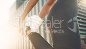 Closeup of one fit mixed race woman standing on one leg for warmup stretches to prevent injury while exercising in urban setting outdoors. Female athlete preparing quads and glutes for training workout or run