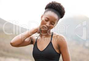 Young african american female suffering from neck pain while working out outside in nature. Unhappy young woman holding her neck in pain while exercising outside.