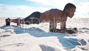 Fit young black man doing plank hold exercises on sand at the beach in the morning. One muscular male bodybuilder athlete with six pack abs doing bodyweight workout to build strong core and endurance