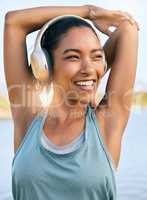 One active latina woman stretching arms and triceps by pulling elbow towards spine while exercising outdoors. Female athlete doing warm up to prepare body and muscles for training workout or run while listening to music on wireless headphones