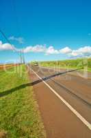 A vehicle in the distance riding on an open highway road leading through agricultural farms. Landscape of growing pineapple plantation field with blue sky, clouds, and copy space in Oahu, Hawaii, USA