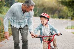 Let go, I can do it. a little boy wearing a helmet and riding a bike outside with his father.