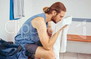 Caucasian player wiping his face with a towel. Tired young player wiping his face after a squash match. Professional athlete taking a break from his squash match to rest in a gym locker room