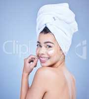 Studio Portrait of a beautiful smiling mixed race woman applying cream to her face. Hispanic model with glowing skin and wet hair against a blue copyspace background