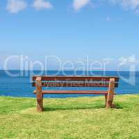 Empty bench overlooking the ocean on a sunny day with copyspace. Wooden seat to sit and reflect, with therapeutic views of patterns in waves and harmony. A peaceful place to have quiet thinking time
