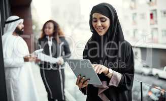 Technology simplifies business. an attractive young businesswoman dressed in Islamic traditional clothing using a tablet on her office balcony.