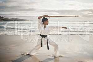 Shes a professional stick fighter. Full length shot of an attractove young female martial artist practicing karate on the beach.