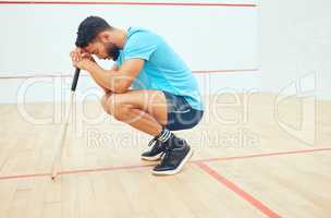 One unknown athletic squash player crouching and feeling sad and stressed after playing game on court. Fit active mixed race athlete feeling anxious after mistake in training practice in sports centre