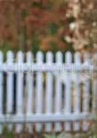 A white classic fence surrounded by green lush plants and trees. Blurred barricade outdoors of a house in the backyard near the garden. Barrier of a home with vibrant flora on a summer day