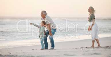 Grandparents bonding with their grandchild. Grandfather talking to his grandchild on the beach. Little girl on holiday with her grandparents. Mature couple on vacation with their grandchild.