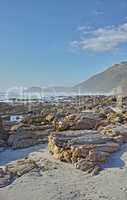 Copyspace at sea with a blue sky background and rocky coast in Camps Bay, Cape Town in South Africa. Boulders at a beach shore with Table Mountain in the horizon on a summer day