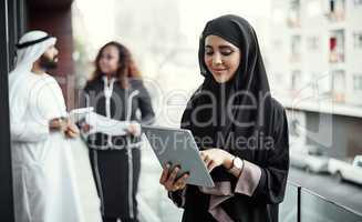 Information at her fingertips. an attractive young businesswoman dressed in Islamic traditional clothing using a tablet on her office balcony.