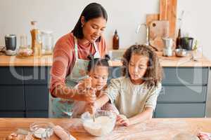 Females only, happy mixed race family of three cooking in a messy kitchen together. Loving black single parent bonding with her daughters while teaching them domestic skills at home