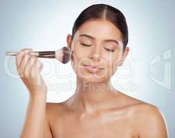 Beautiful woman holding and using cosmetic makeup brush to apply blush makeup while posing with copyspace. Caucasian model isolated against grey studio background. Getting ready after skincare routine