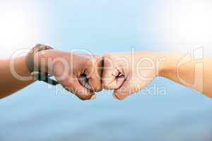 Female friends feeling supported, united and touching fists at the knuckles. Feeling motivated and ready to achieve. Closeup of two unknown people giving each other a fist bump against blue copyspac