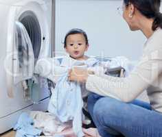 Mom always has time for fun. a young mother playfully bonding with her baby girl while doing the laundry at home.