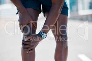 African american athlete taking a break from running to touch his knee and inspect an injury. Fit, sporty, healthy man feeling pain in his knee joint during a jog in the city. Athlete working out
