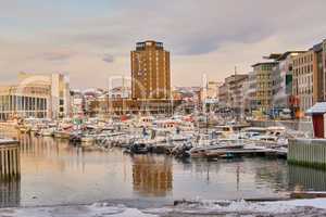 Boats and yachts docked in a harbor with the city in the background in Bodo, Norway. Sea vessels at a port in the ocean ready to depart for a cruise in the travel and tourism industry at dusk