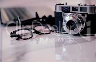 Closeup of a camera and glasses on a desk in an office. Blogger or photographers workstation at home of in a modern office