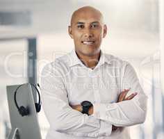 Portrait of one confident mature mixed race call centre telemarketing agent standing with arms crossed while working in a call centre. Happy male manager and supervisor operating helpdesk for customer service and sales support
