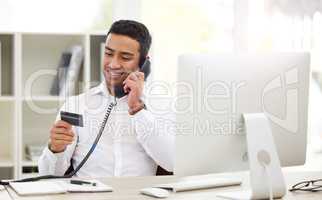 I need to use my card. a young businessman using a landline and credit card in an office at work.