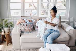 Not a single stain in sight. Shot of an attractive young woman sitting alone in her living room and folding baby clothes.
