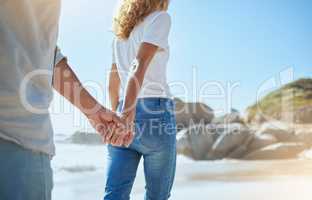 Closeup of a loving mature couple holding hands while walking on the beach in summer. Affectionate husband and wife enjoying stroll by the sea while on holiday. Man and woman on a relaxing date