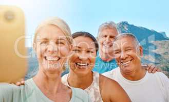 Group of active seniors posing together for a selfie or video call on a sunny day against a mountain view background. Happy retirees exercising together outdoors. Living healthy and active lifestyles