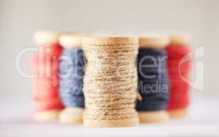 Many rolls of coloured yarn or string lined up in a row in studio isolated against a grey background. For the production of textiles, sewing, crocheting, knitting, weaving, embroidery or rope making