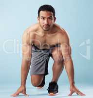 Fullbody young hispanic man standing on his mark in studio isolated against a blue background. Mixed race shirtless male runner ready to race, sprint or long distance. Endurance and cardio training